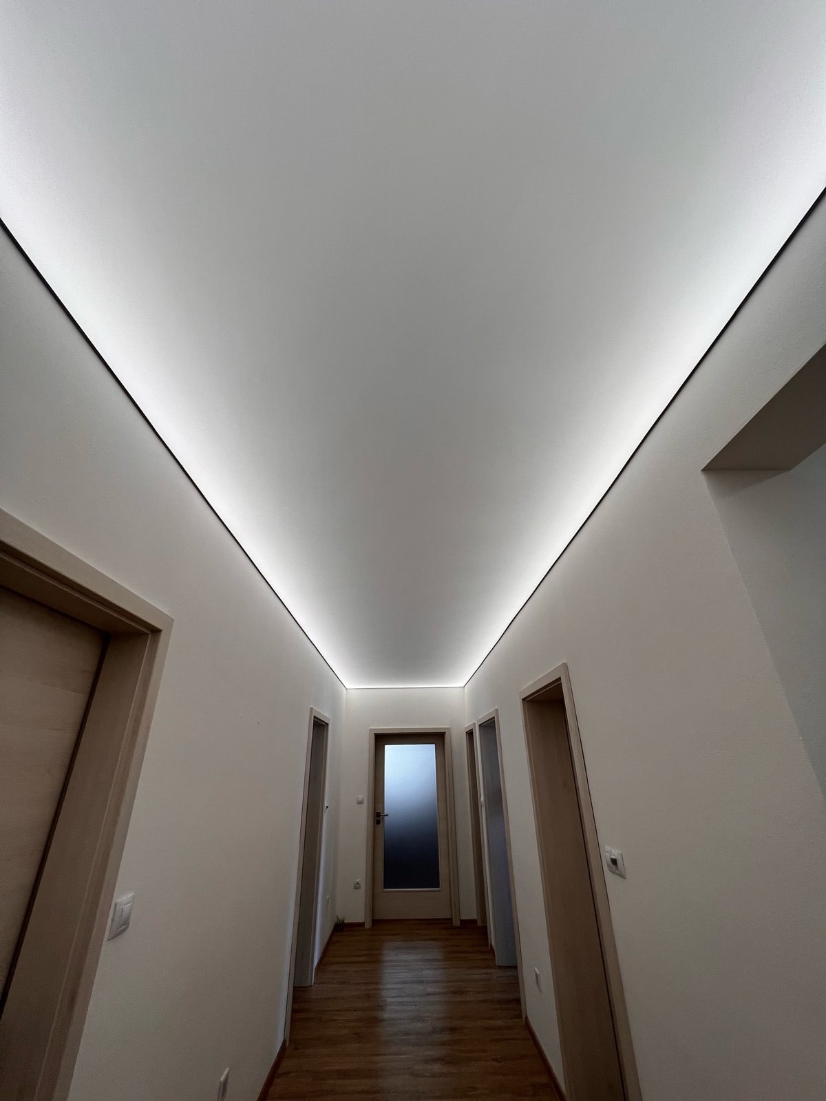 Moderní chodba s napnutým stropem a integrovaným LED osvětlením vytvářejícím elegantní světelný design.