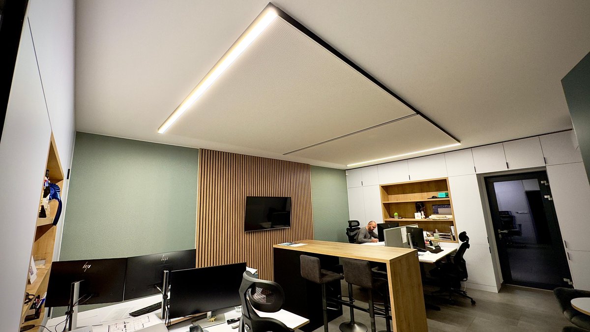 Moderní kancelářský prostor s napínaným stropem, integrovaným LED osvětlením a akustickou zelenou stěnou s dřevěnými lamelami.